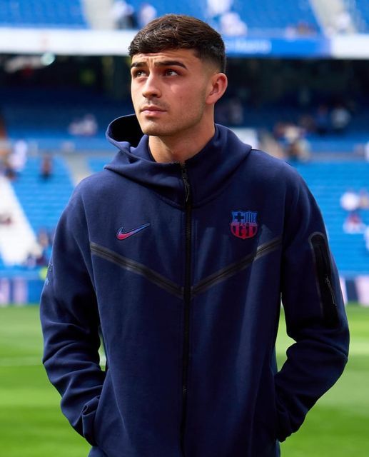 a man standing on top of a soccer field wearing a blue jacket and black pants