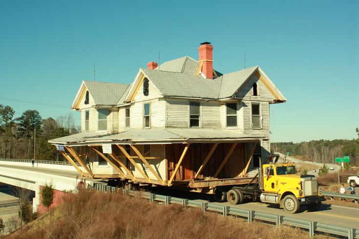 a house being moved down the road by a yellow truck with it's flatbed