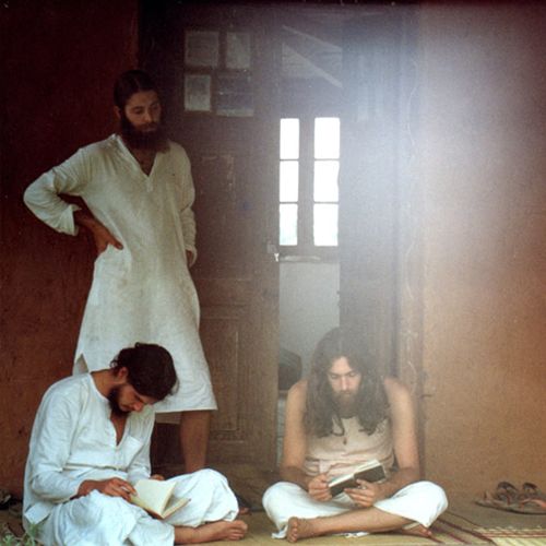 two men sitting on the floor in front of a door while another man looks at his cell phone