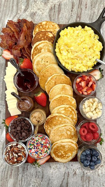a breakfast platter with pancakes, bacon, eggs, fruit and other foods