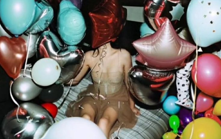 a woman sitting in the middle of balloons and streamers on her head, surrounded by other balloons