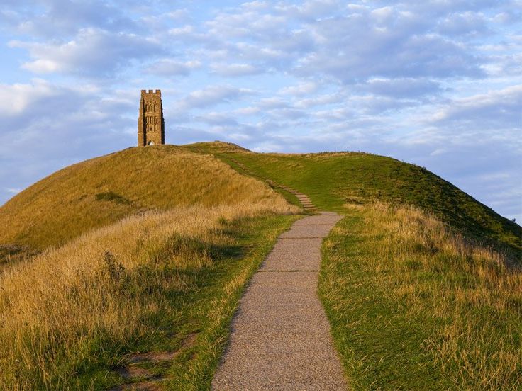 a path leading to a tower on top of a hill with grass growing up the side