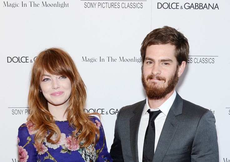 a man and woman standing next to each other in front of a white wall with flowers on it