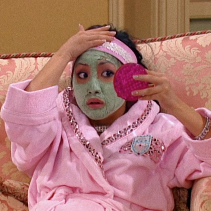 a woman sitting on top of a couch holding a pink object in her hand and wearing a green face mask