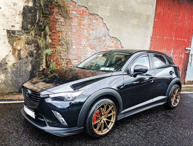 a black and gold mazda cx - 3 parked in front of a red door
