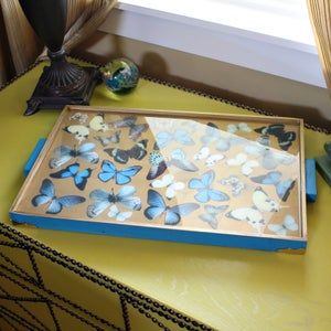 a blue and gold tray with butterflies on it sitting on a yellow table next to a lamp