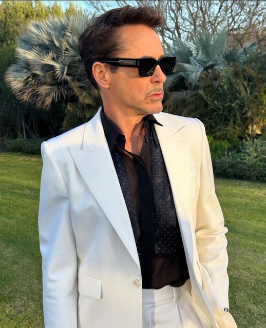 a man in a white suit and sunglasses standing on the grass with his hands in his pockets