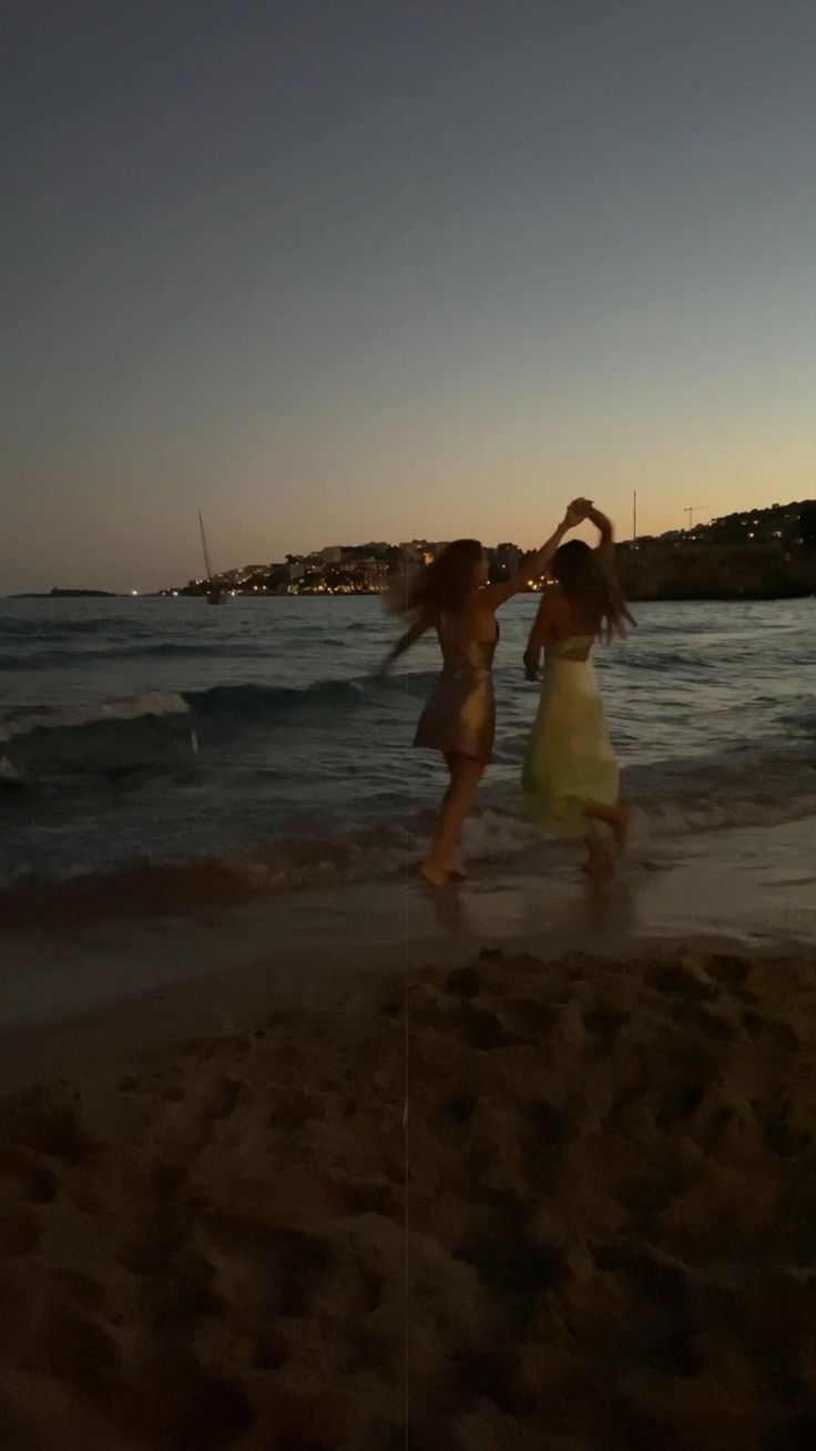 two girls are playing on the beach at sunset