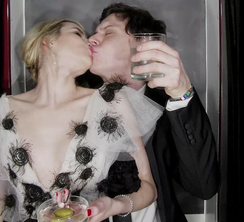 a man and woman kissing while holding drinks