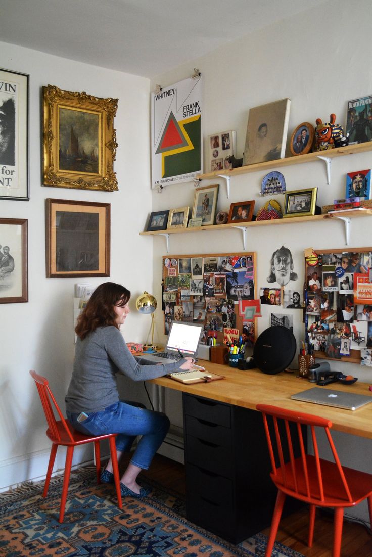 a woman sitting at a desk in front of a wall with many pictures on it