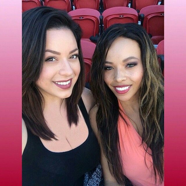 two beautiful young women standing next to each other in front of a stadium filled with red chairs