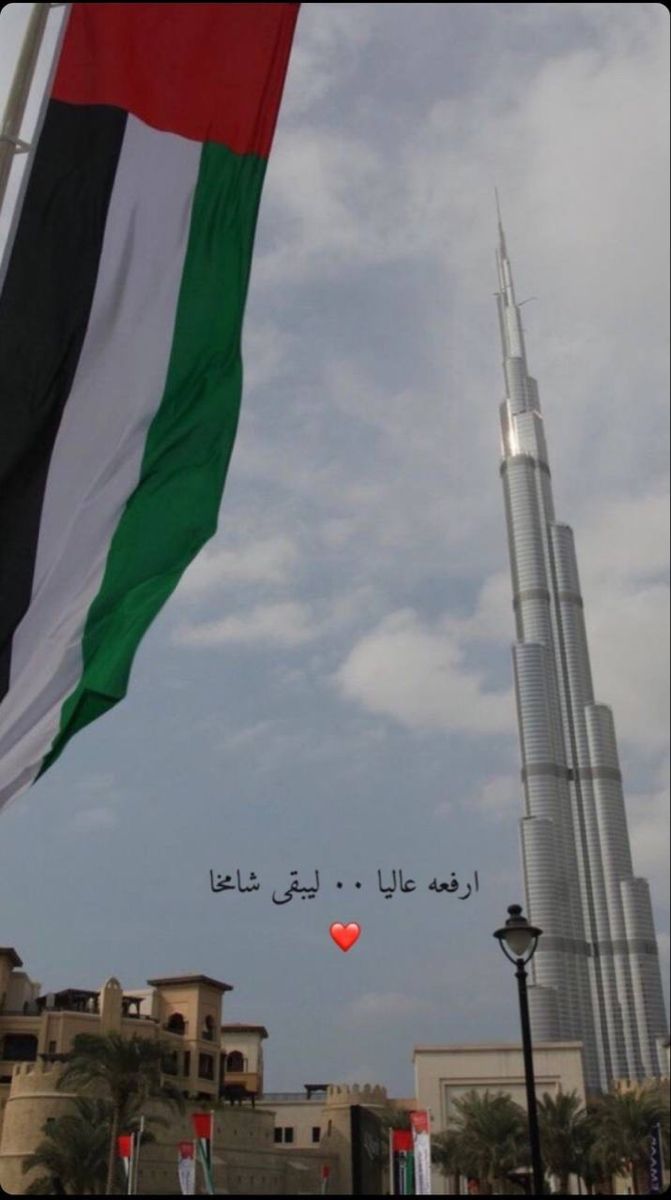 a flag flying in the air next to a tall building with a heart on it