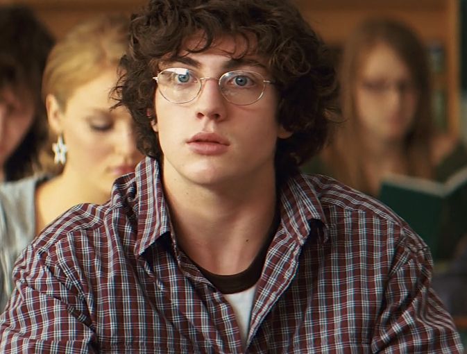 a young man with glasses sitting in front of other people