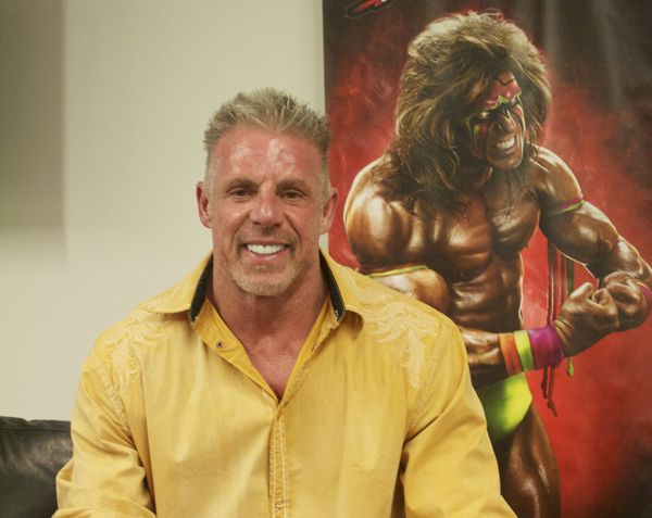 a man in yellow shirt sitting next to a large wall with an image of a wrestler on it