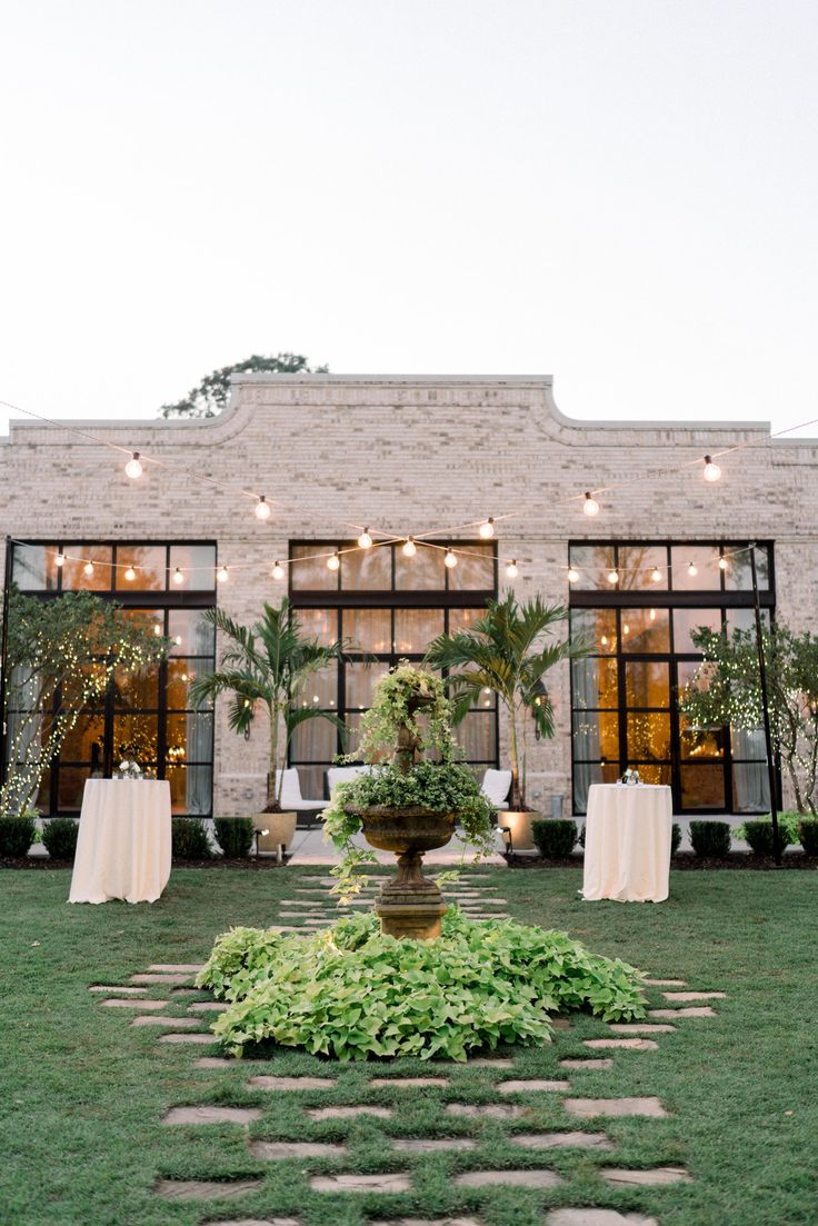 an outdoor venue with tables and chairs set up in front of the building, surrounded by greenery