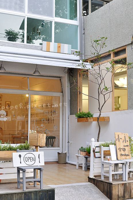 an outside view of a store front with wooden benches and plants in the foreground