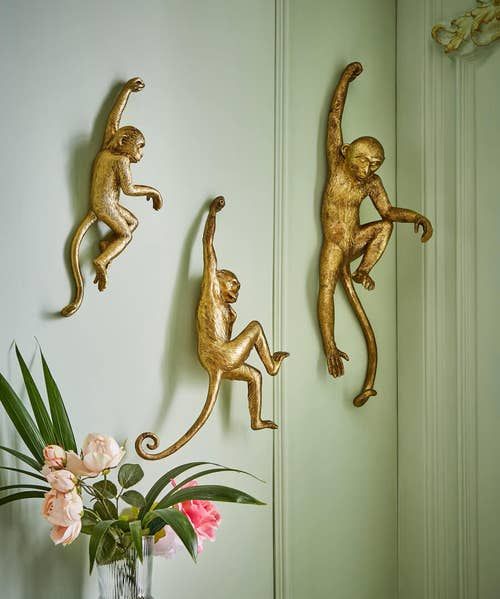 three gold monkeys are hanging on the wall next to a vase with flowers in it