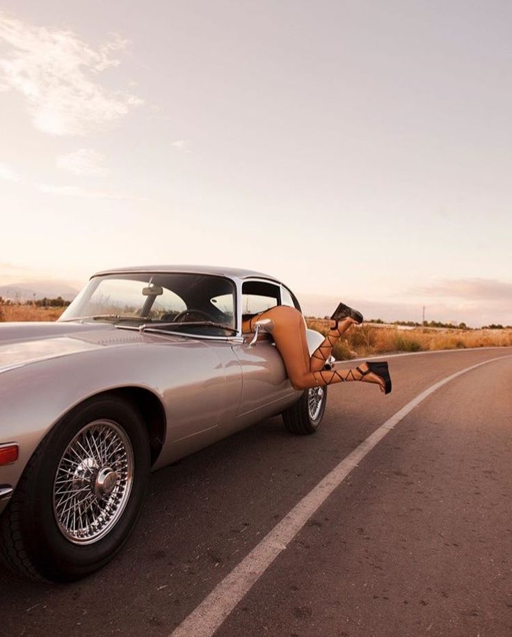 a woman laying on the hood of a sports car with her legs up in the air