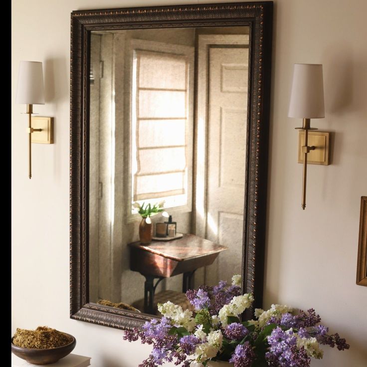 a large mirror hanging on the wall next to a vase with flowers in front of it