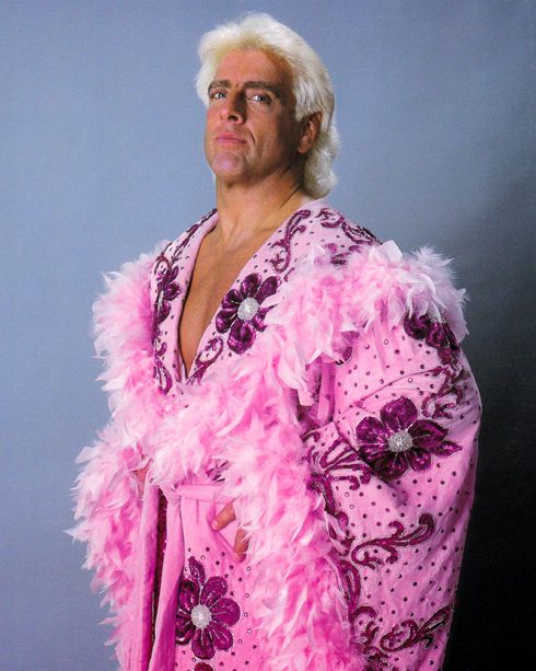 a man dressed in pink and purple is posing for a photo with feathers on his jacket