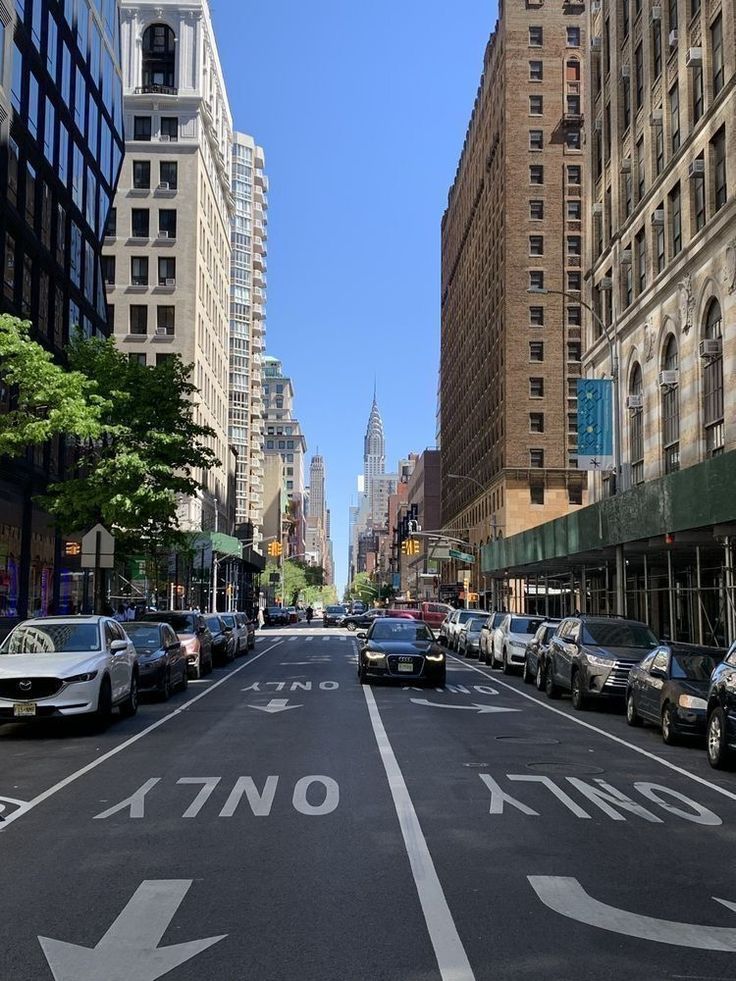 an empty city street with several cars parked on both sides and buildings in the background