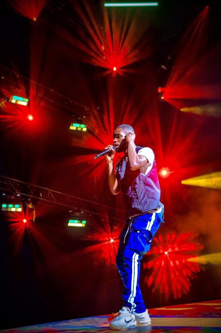 a man standing on top of a stage holding a microphone in front of red and yellow lights