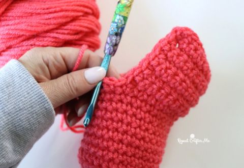 a woman holding a crochet hook in front of a red knitted mitt