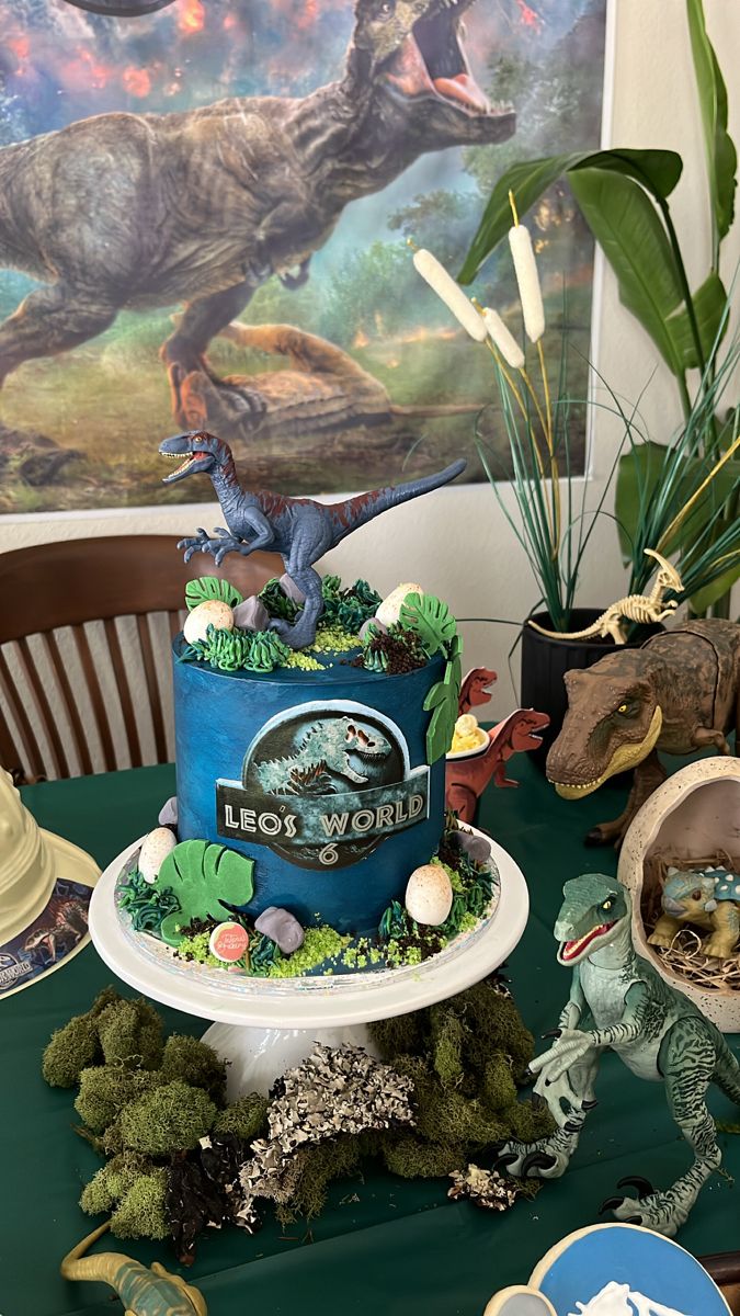 a dinosaur themed birthday cake on top of a table with other dinosaurs and plants in the background