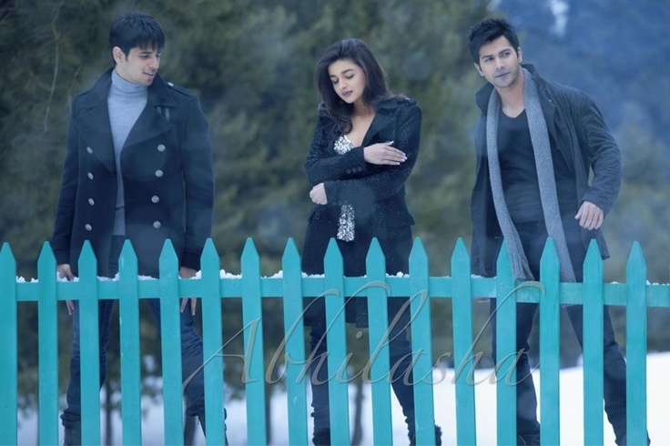 three people standing next to each other near a blue fence and snow covered ground with trees in the background