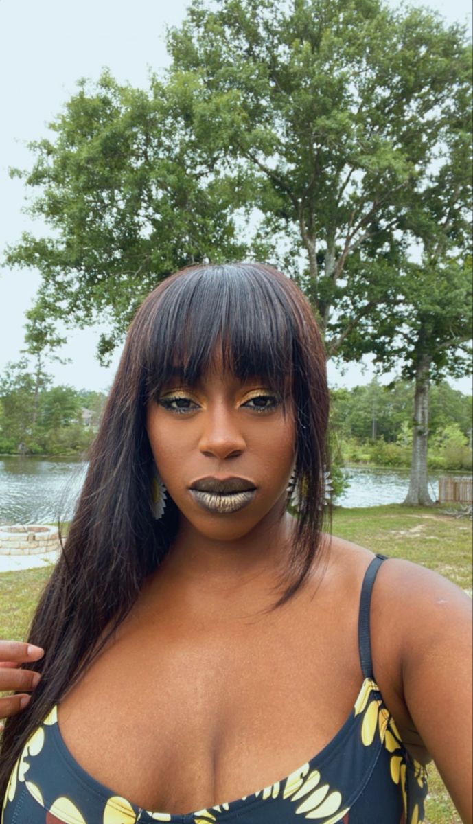 a woman with makeup on her face posing for the camera in front of some trees