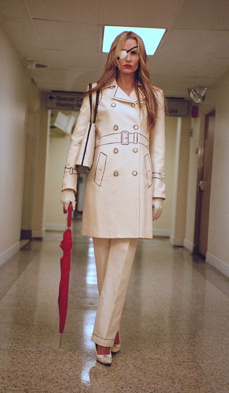 a woman with an umbrella walks down a hallway in a trench coat and matching heels