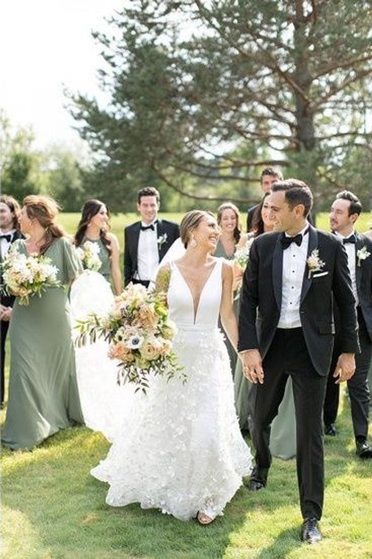 a bride and groom walk through the grass with their bridal party in the background