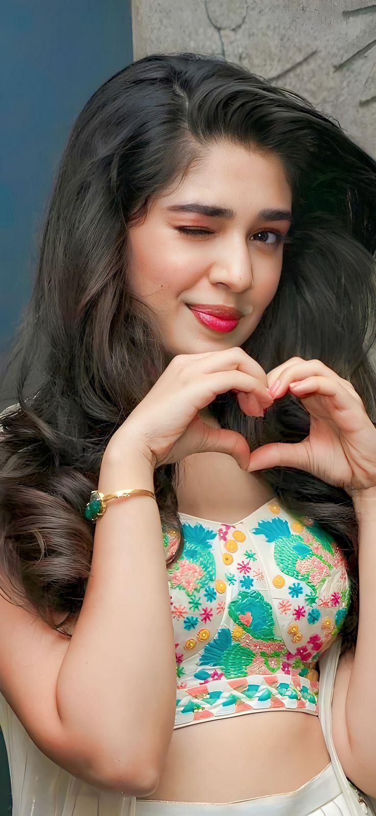 a woman making a heart shape with her hands while standing in front of a wall