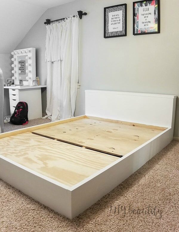 a bedroom with a bed frame made out of plywood and carpeted flooring