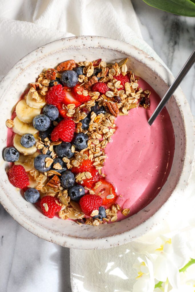 a bowl filled with fruit and granola on top of a white cloth next to flowers