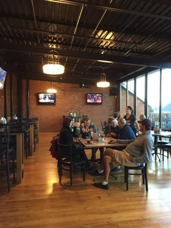 people sitting at tables in a restaurant with large windows and televisions on the wall