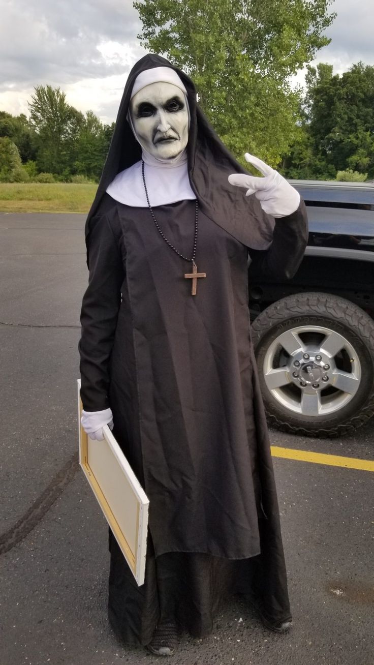 a man dressed in a nun costume standing next to a black truck with a cross on it