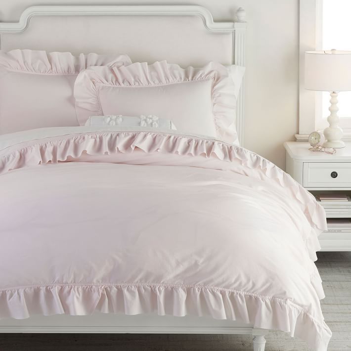 a white bed with pink ruffled sheets and pillows on top of the headboard