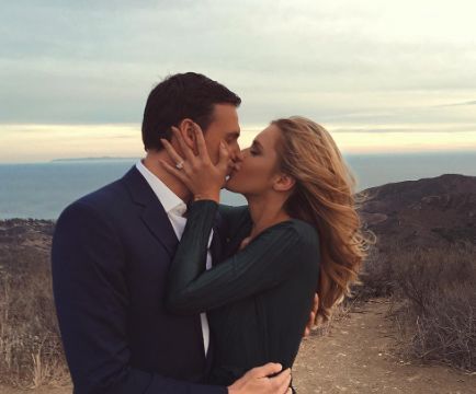 a man and woman kissing each other in front of a mountain range with the ocean in the background