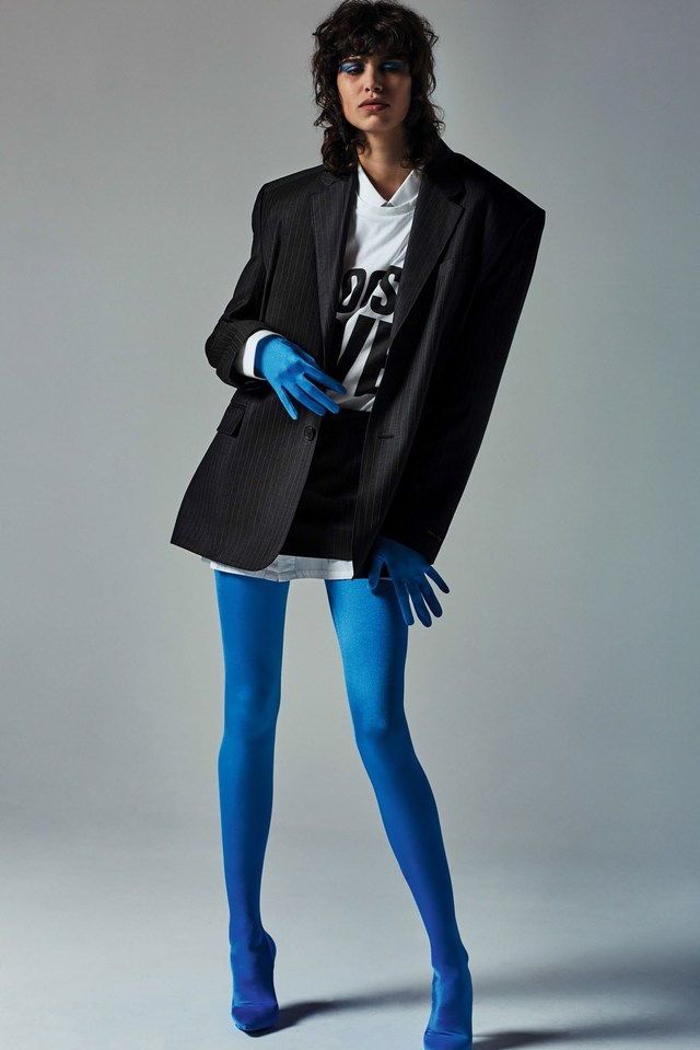 a woman in blue tights and a black blazer is posing with her hands on her hips