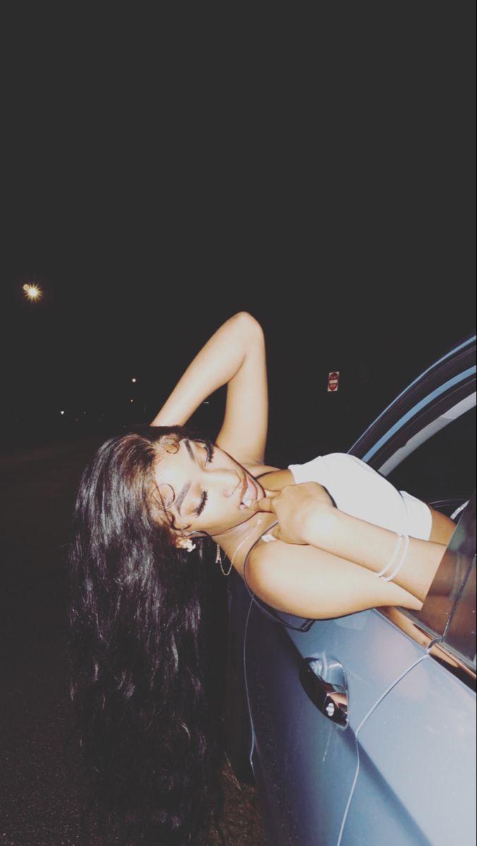 a woman leaning on the side of a car at night with her head hanging out