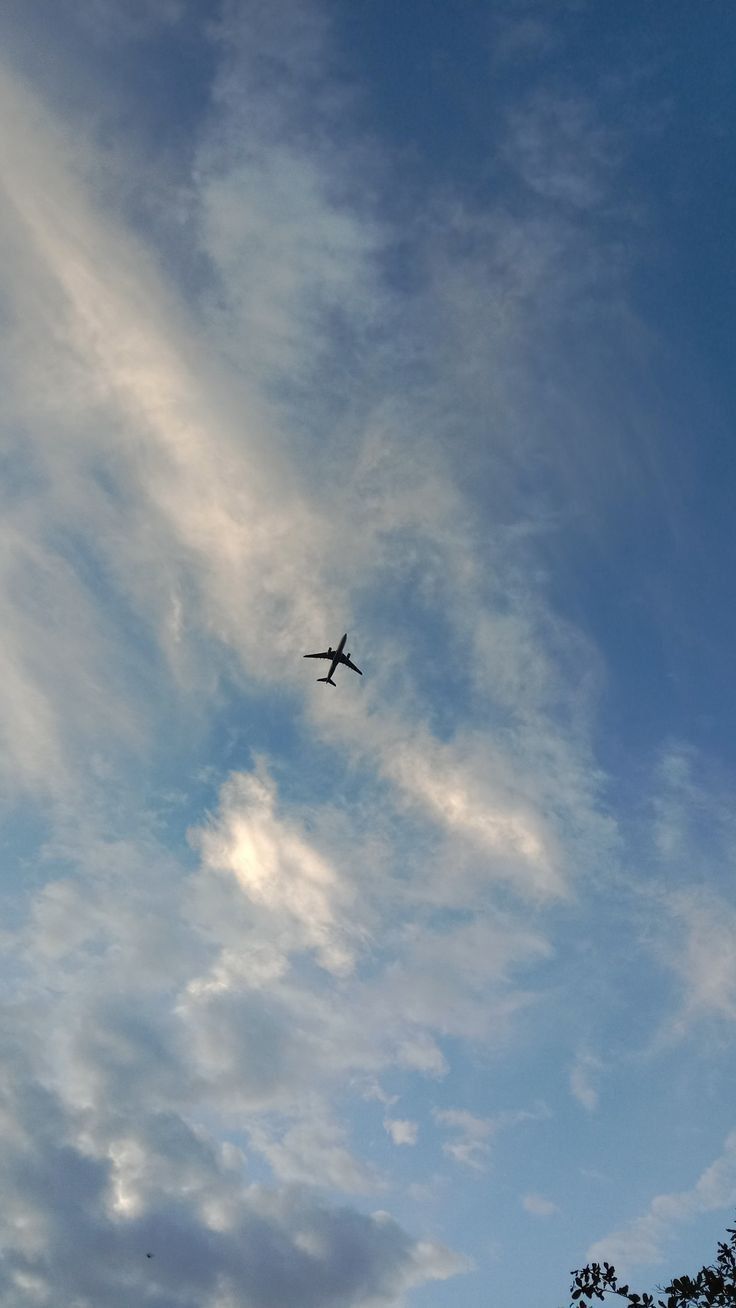 an airplane is flying high in the blue sky with white clouds and trees below it