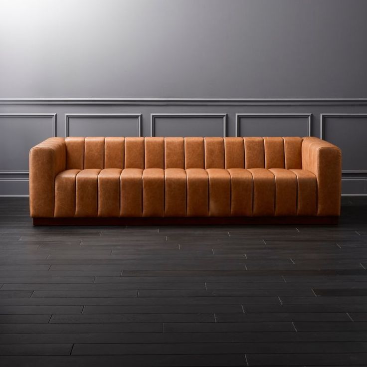 a brown couch sitting on top of a hard wood floor next to a gray wall