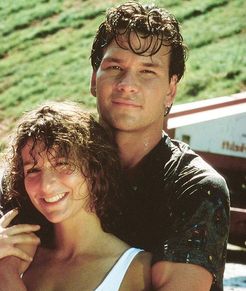 a man and woman standing next to each other in front of a green hillside with grass