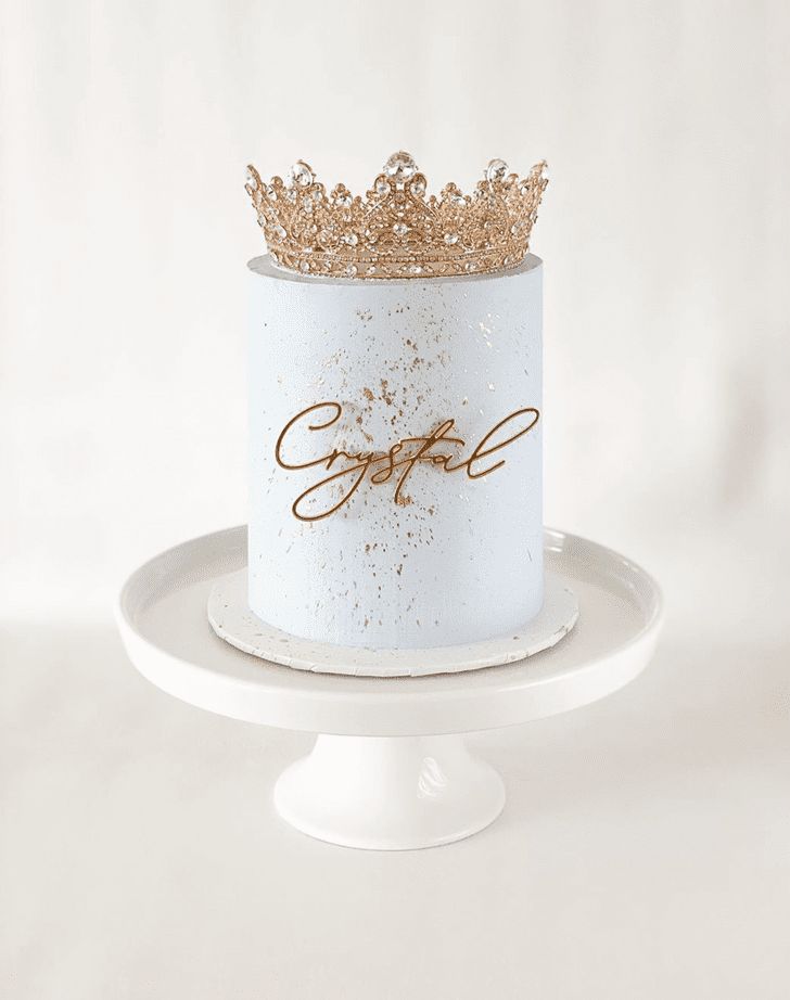 a white cake with gold lettering and a crown on top is sitting on a plate