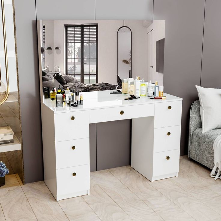 a white dressing table with drawers, mirror and bottles on it in front of a couch