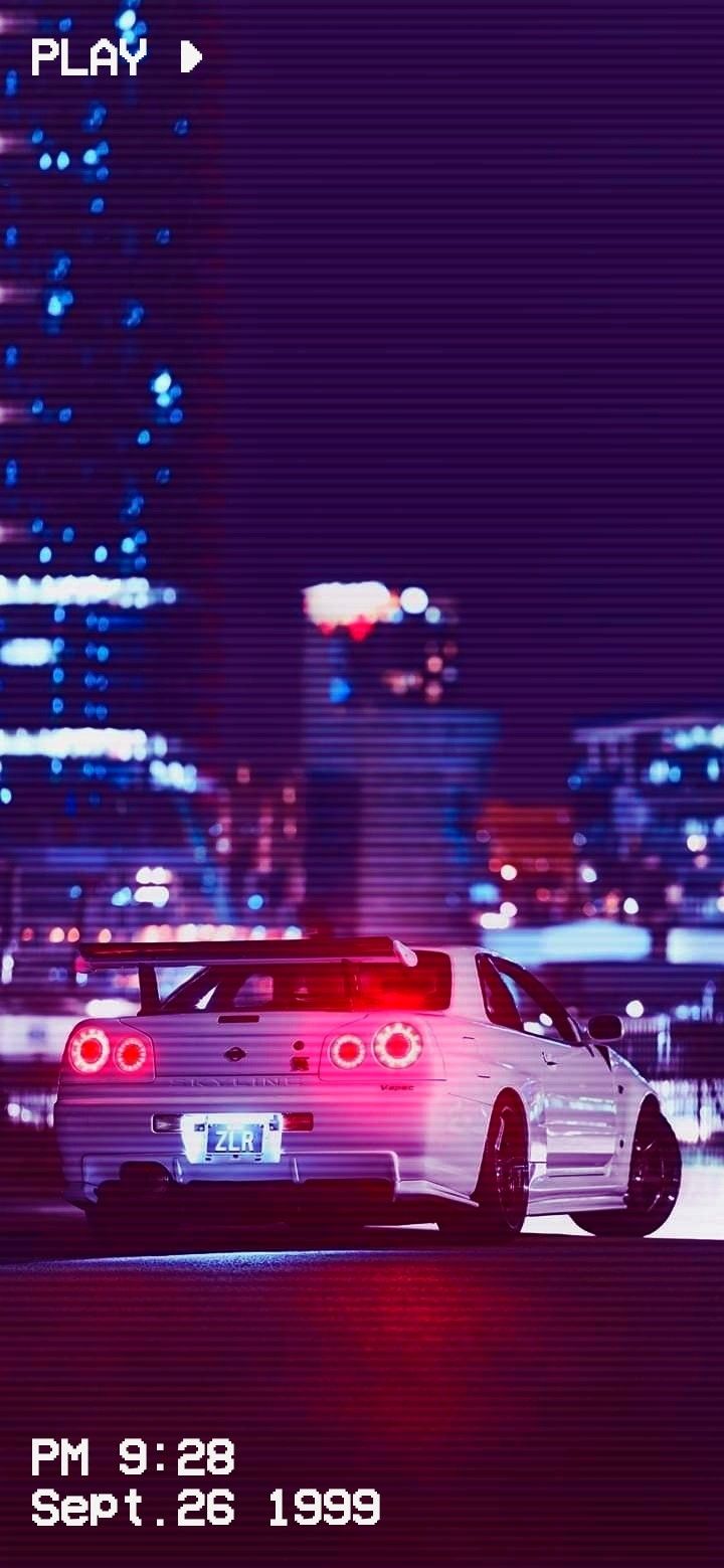 a white car parked in front of a tall building with city lights behind it at night