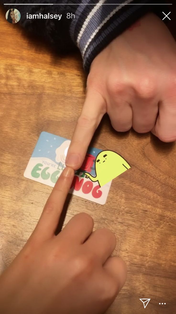 a person pointing at a sticker on top of a wooden table next to another hand