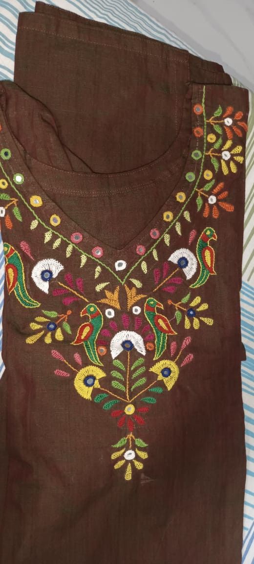 a brown shirt with colorful embroidered designs on the front and back, sitting on a bed