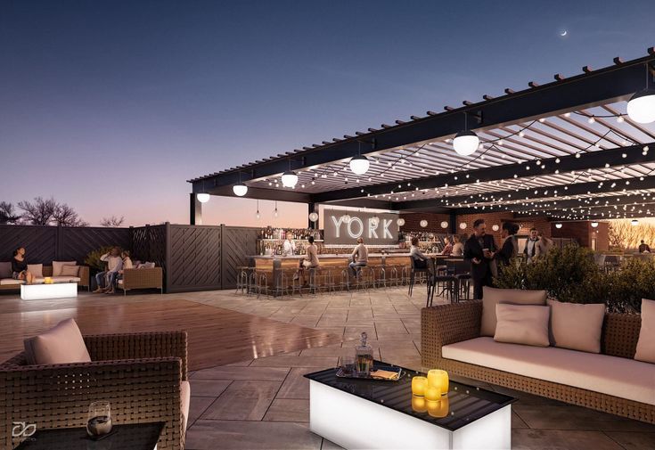 an outdoor patio with seating and lights on the roof at night, surrounded by potted plants